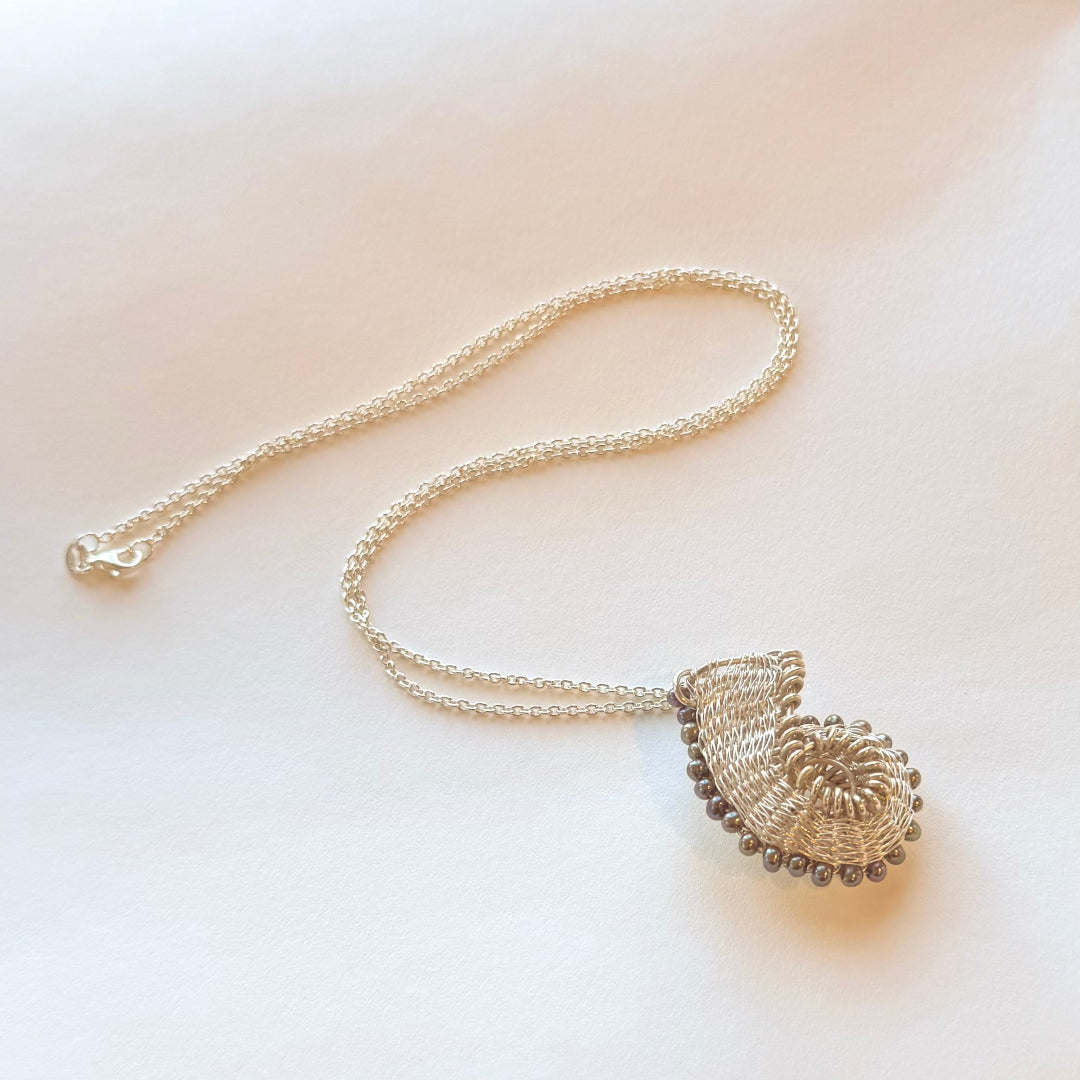 Silver wire-wrapped pendant with blue pearls on a light background