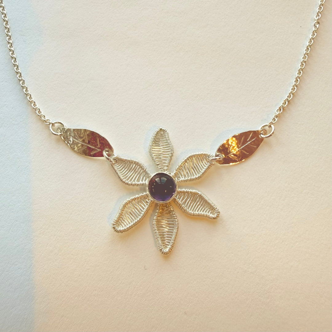 Silver flower-shaped necklace with a central gemstone on a beige background