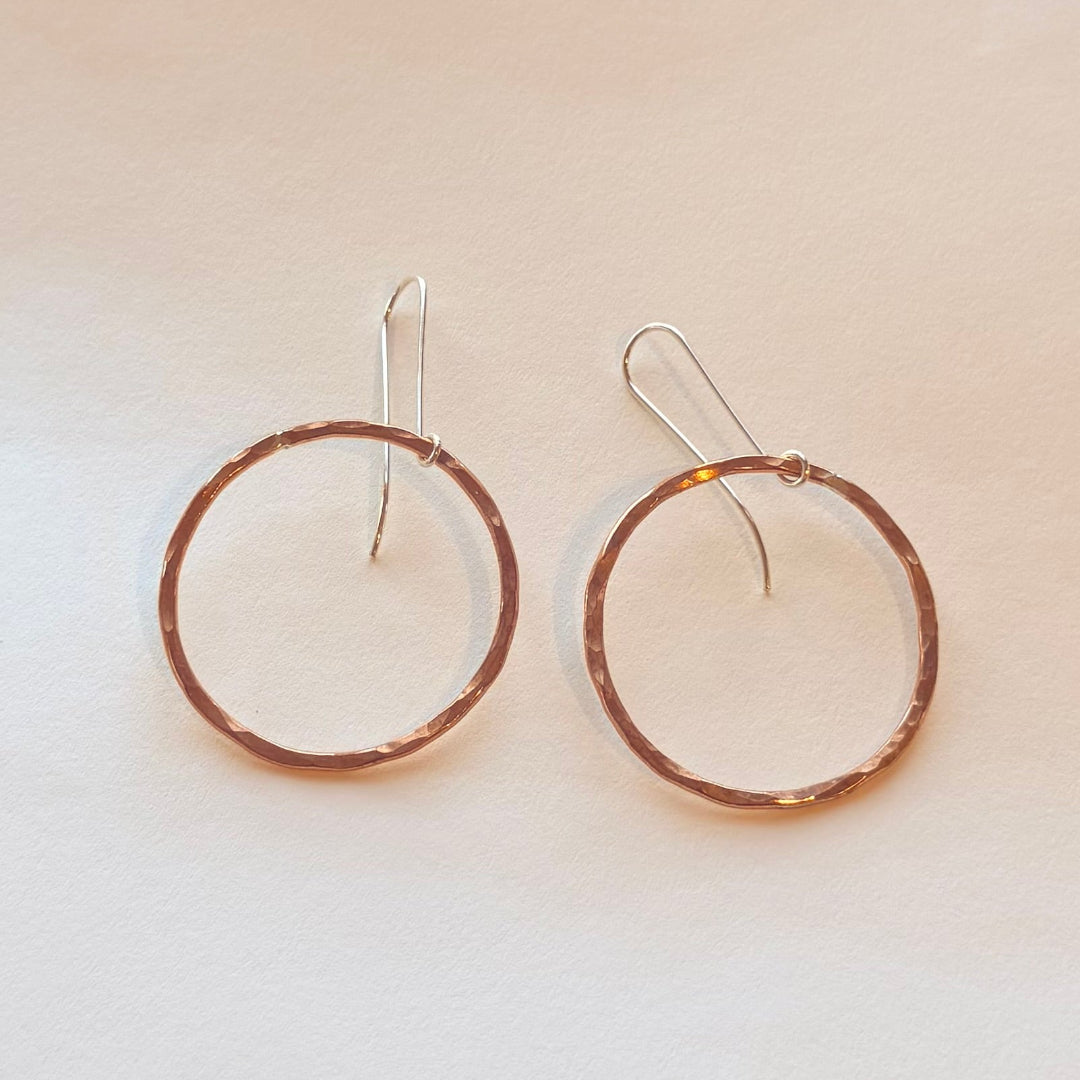 Pair of copper hoop earrings with silver hooks on a light beige background