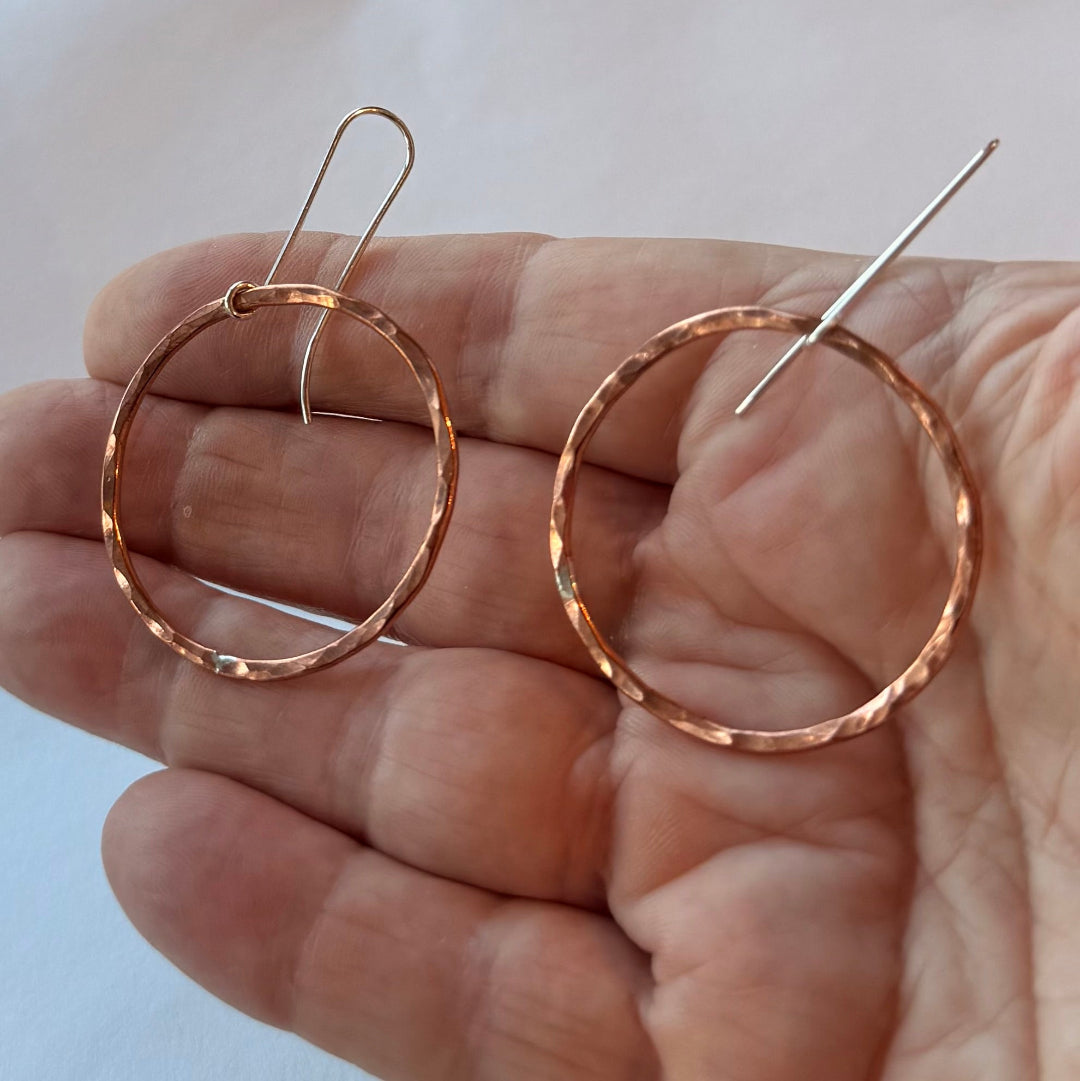 Copper & silver hoop earrings held in a hand against a light background
