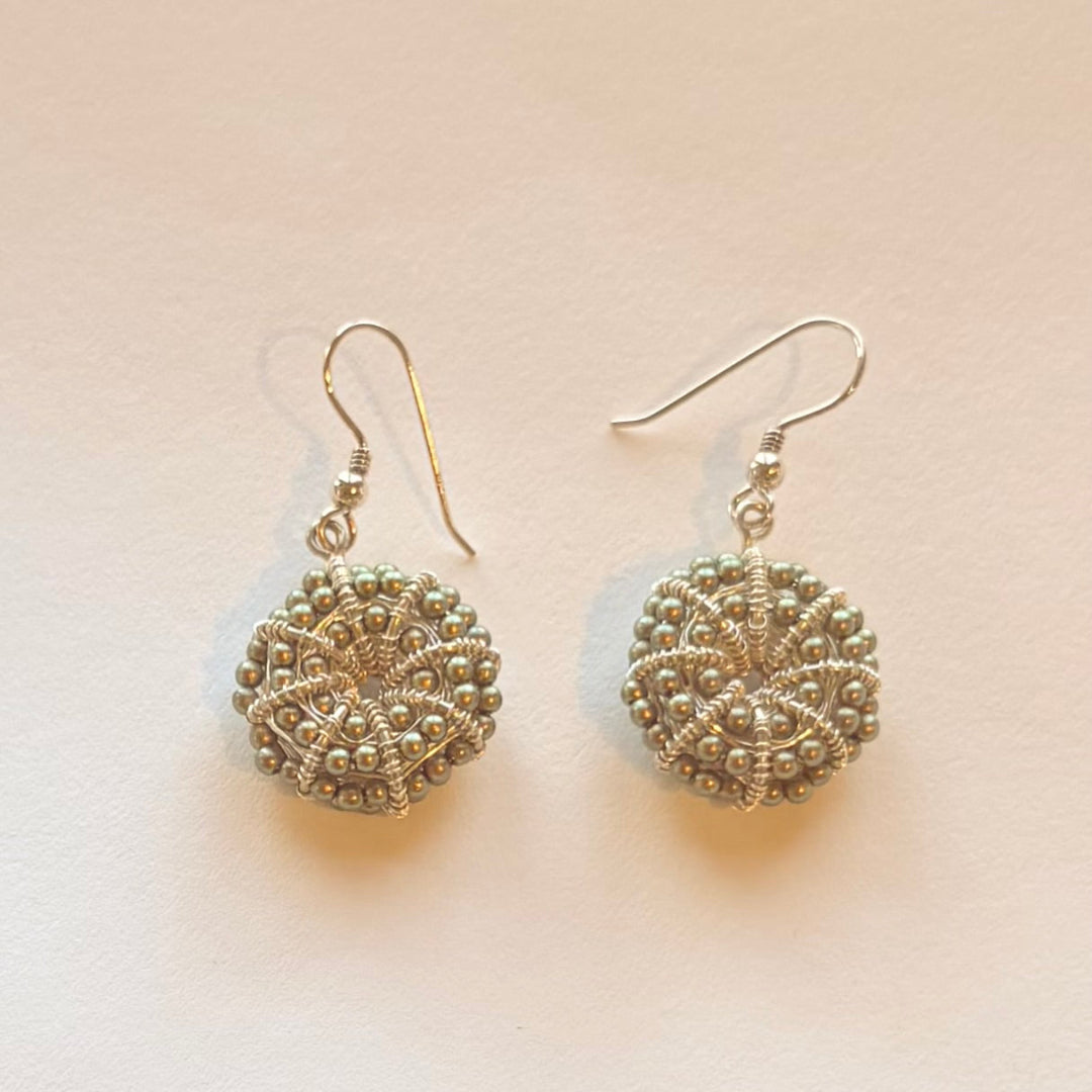 Pair of silver & green pearl kina shaped earrings on a beige background
