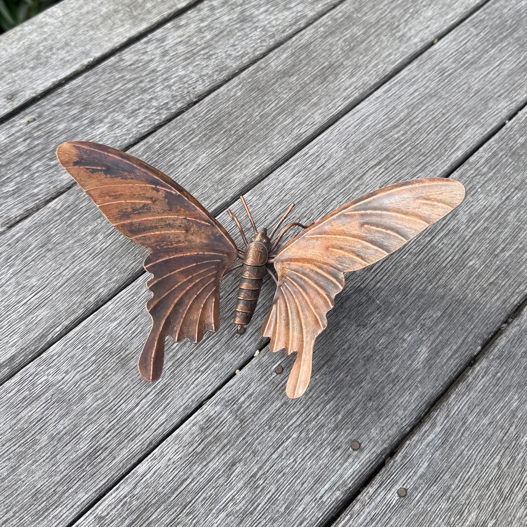 Copper butterfly sculpture with coin body on a wooden surface