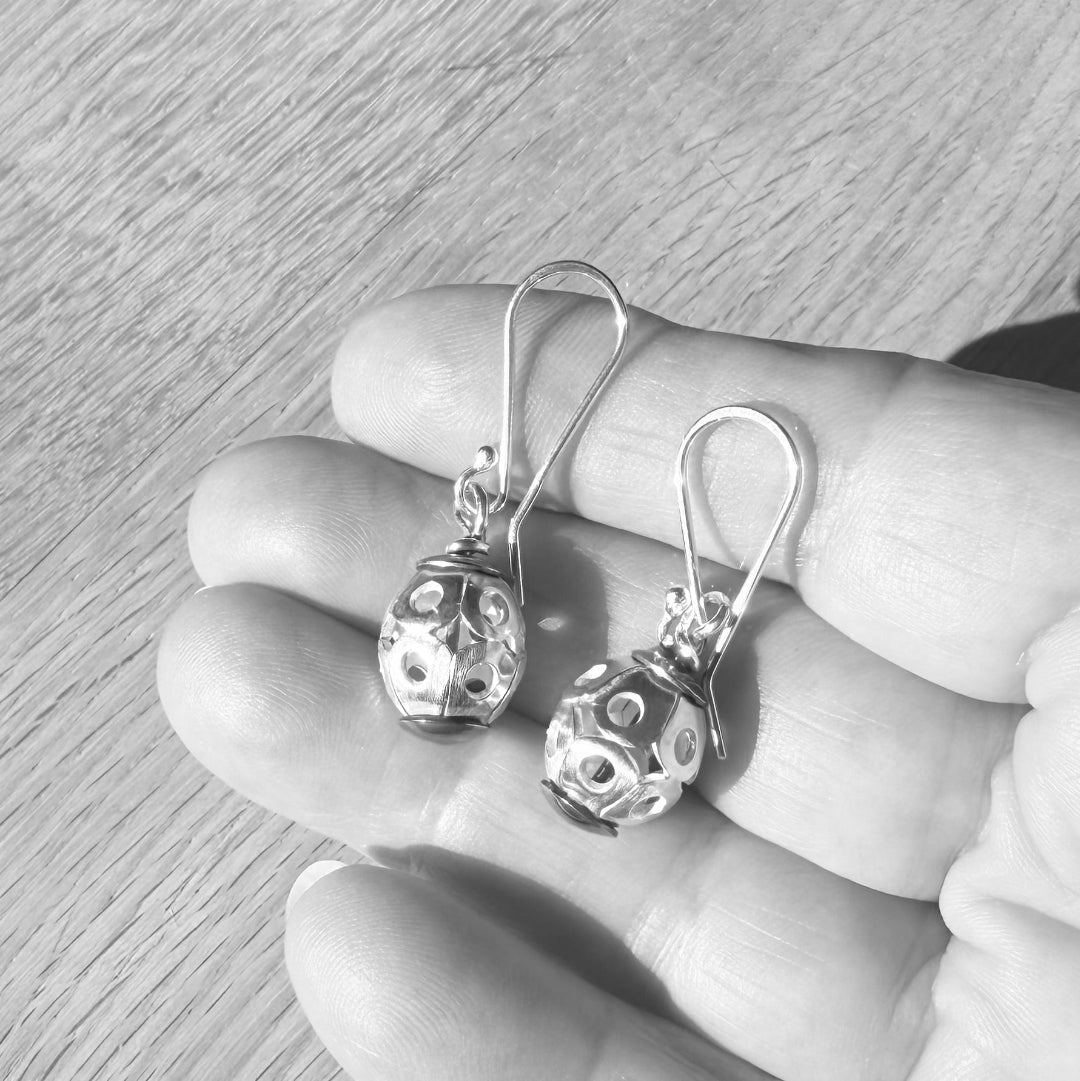Silver earrings held in a hand on a wooden surface
