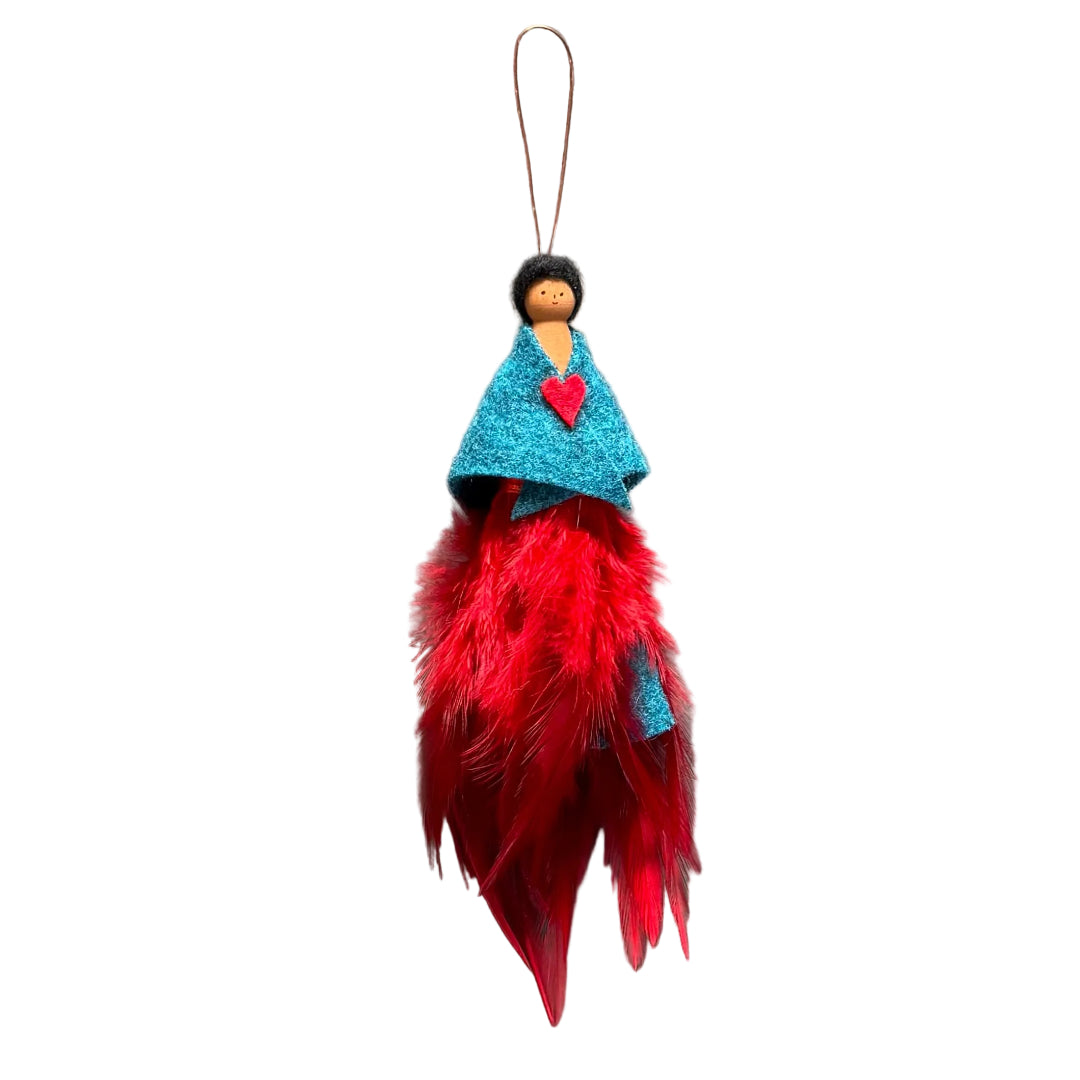 A handmade decorative ornament featuring a small peg doll with black hair and a face, dressed in a turquoise felt shawl with a red felt brooch, and finished with a long red feather skirt hanging from a copper wire, set against a white background.