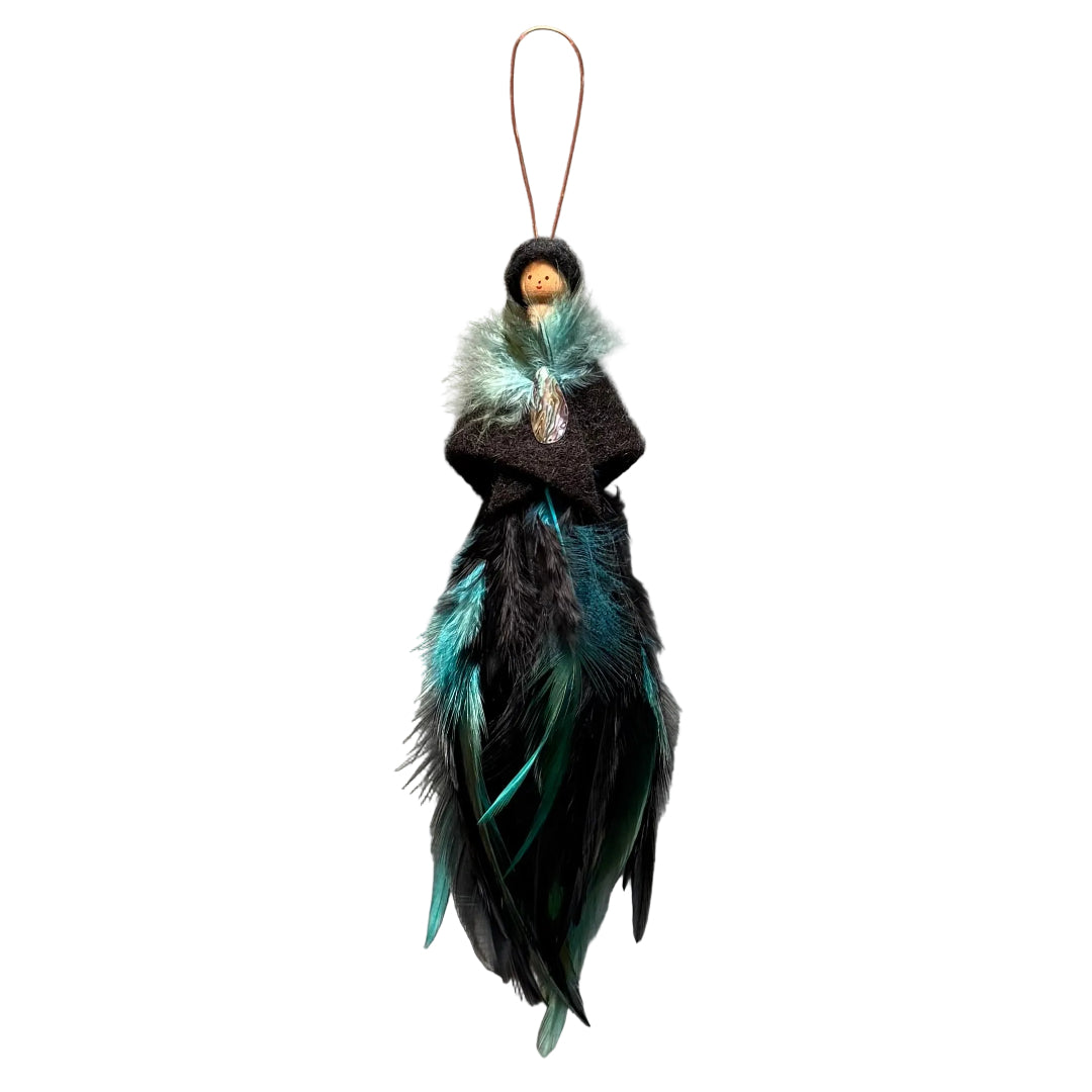 A handmade feather ornament featuring a small dark brown fabric peg doll with a wooden bead head and a copper wire hanging loop, decorated with black and teal feathers on a white background.