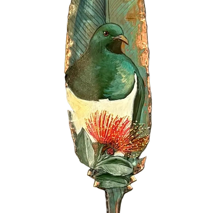 Close up of a copper wall sculpture shaped like a feather, featuring a painted green and white Kereru bird with a red-orange flower, mounted on a white wall.