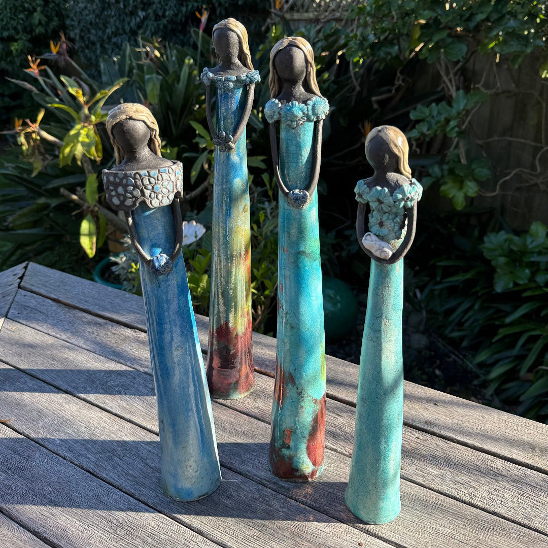 Four tall ceramic garden figurines with distressed blue, turquoise, and brown glazes, displayed on a wooden deck with a garden background.