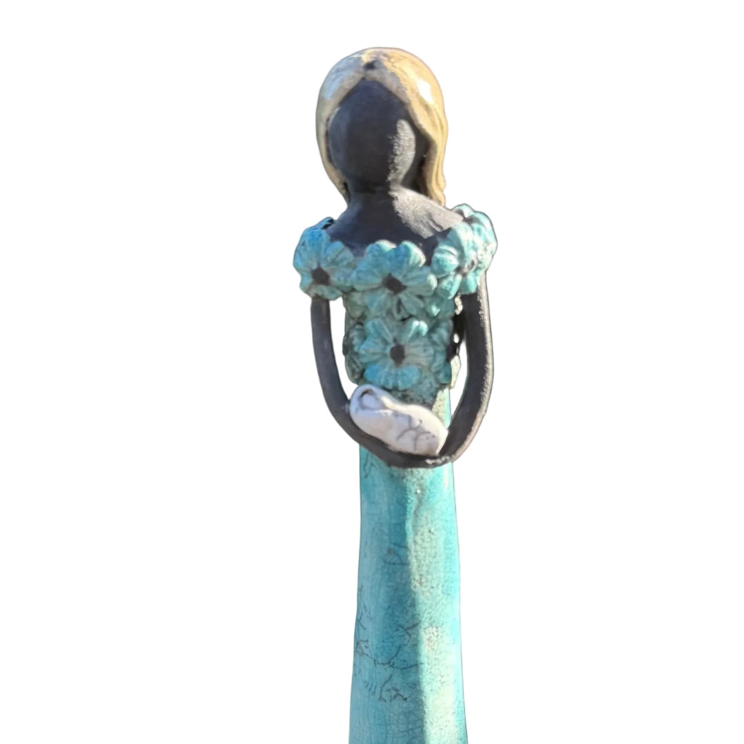 A decorative figurine of a woman with blonde hair, wearing a long teal dress and holding a baby.