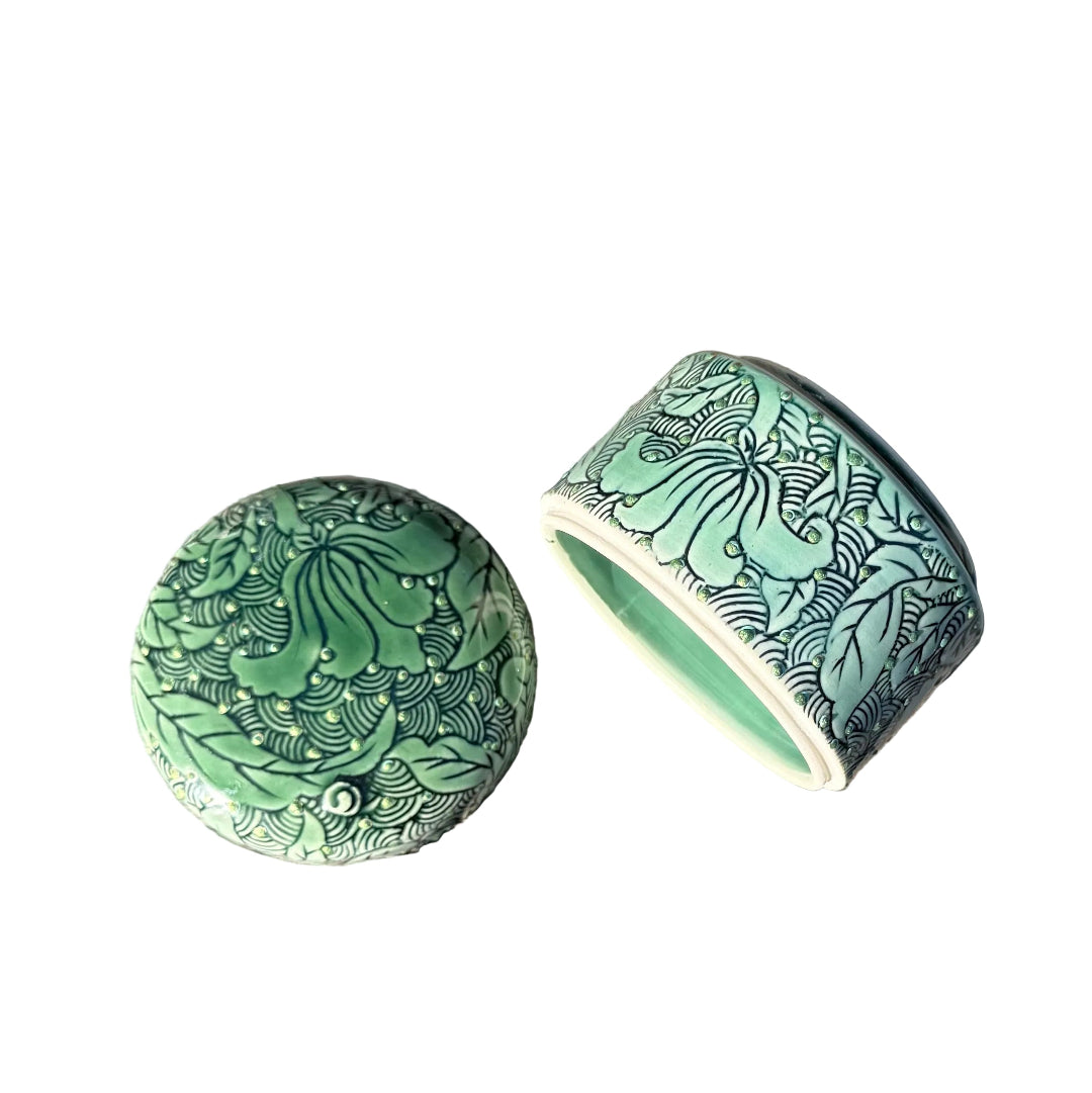 Green ceramic lid & base with black floral lotus patterns, one round lid and one cylindrical base, displayed on a white surface.