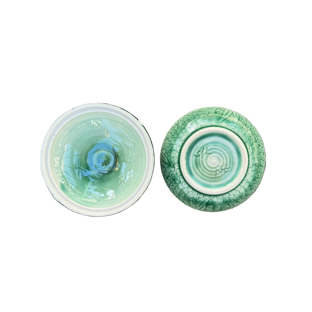 Inside lid & base of green ceramic trinket dish showing the patterned & signed bottom on a white surface.