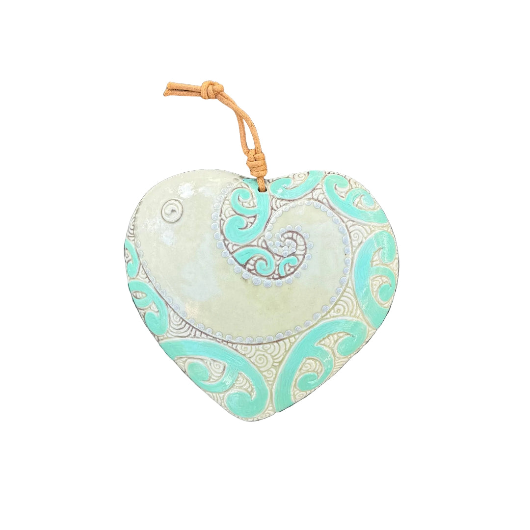 A heart-shaped ceramic wall hanging ornament with a spiral seashell design in mint green, cream, and brown, hanging on a white wall.