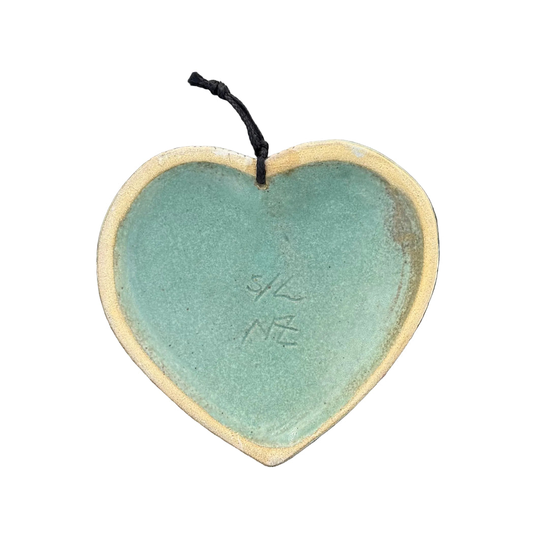 Back view of a heart-shaped ceramic wall hanging ornament with a cream rim and a pale green glazed center, signed S/L NZ.
