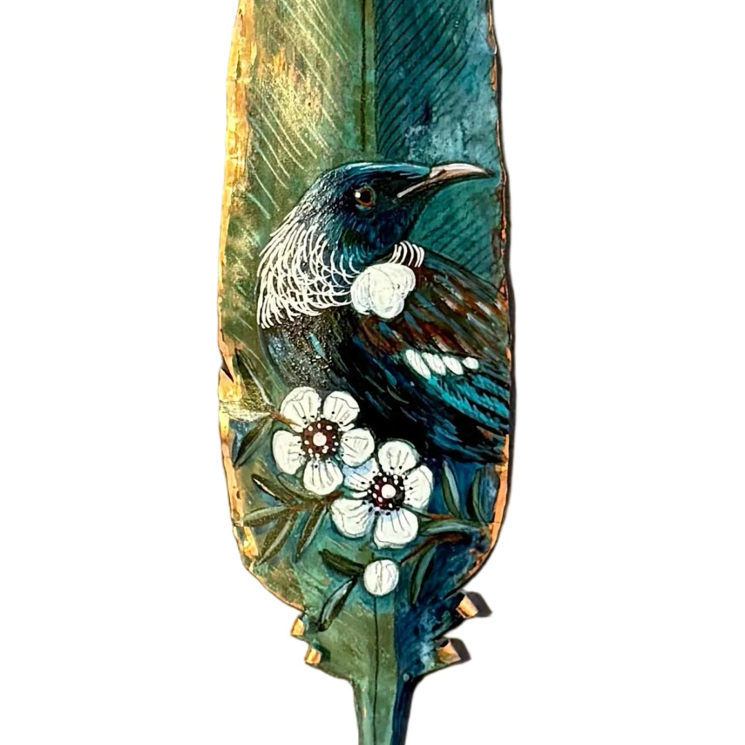 Close up view of a copper feather wall art hand painted with a Tui bird on Manuka flowers against a white background.
