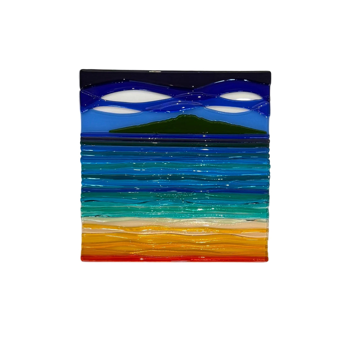 A framed abstract landscape art piece featuring layered horizontal bands of deep blue, teal, green, orange, and red, set within a white frame on a light wood background.