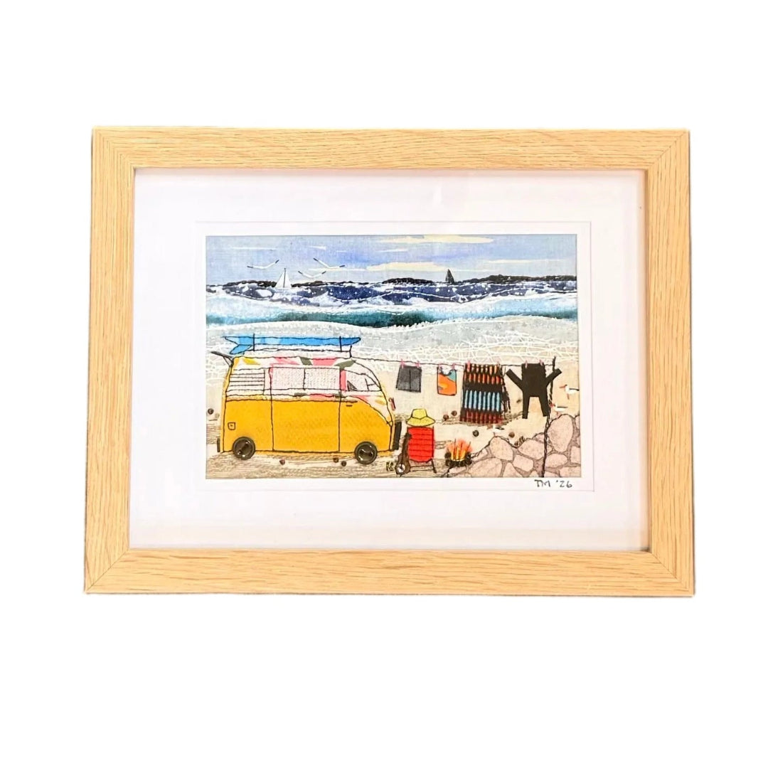 A small framed textile artwork depicting a yellow combi van by the sea, on a white background.