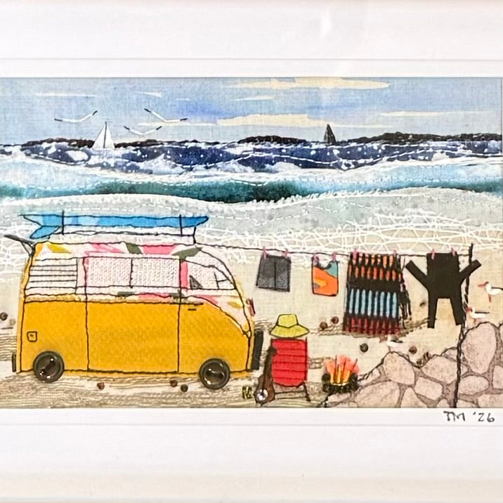 A whimsical beach scene textile artwork featuring a yellow van with a blue surfboard, a red beach chair, colorful hanging towels, and a small campfire, set against a blue ocean and white surf. The piece is signed 'TM '26' in the lower right corner.