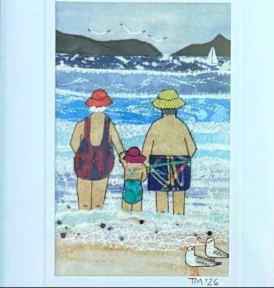 A close up of a small framed textile artwork with a colourful coastal depiction on a white background.