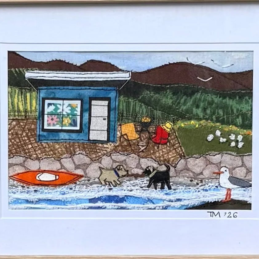 Close up of a small textile landscape artwork depicting a blue bach on a white background.