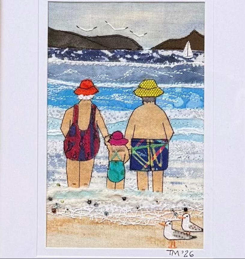A close up of a small framed textile artwork with a colourful coastal depiction featuring a family of 3 paddling in the waves on a white background.