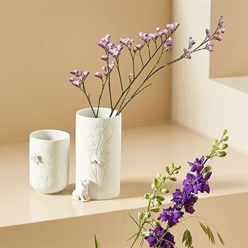 White vase with purple flowers on a beige shelf