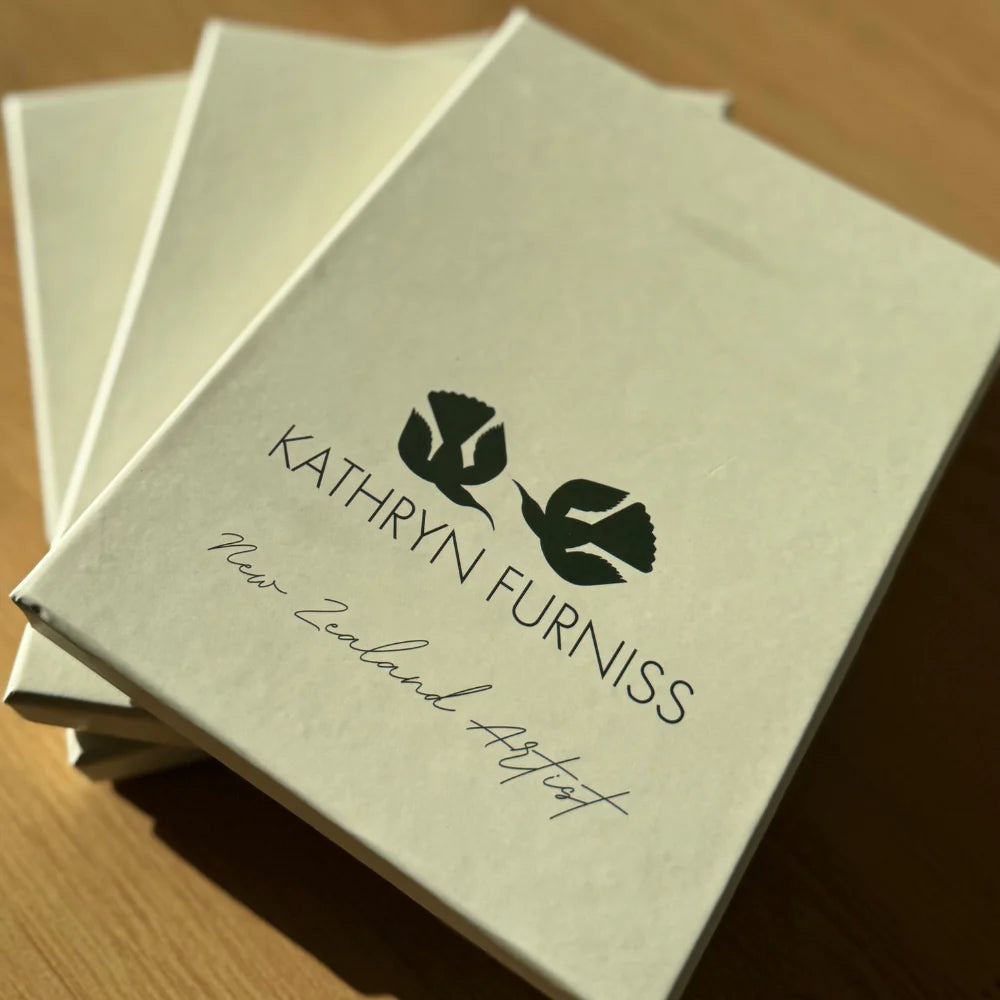 Stack of beige boxes with 'Kathryn Furniss' branding on a wooden surface