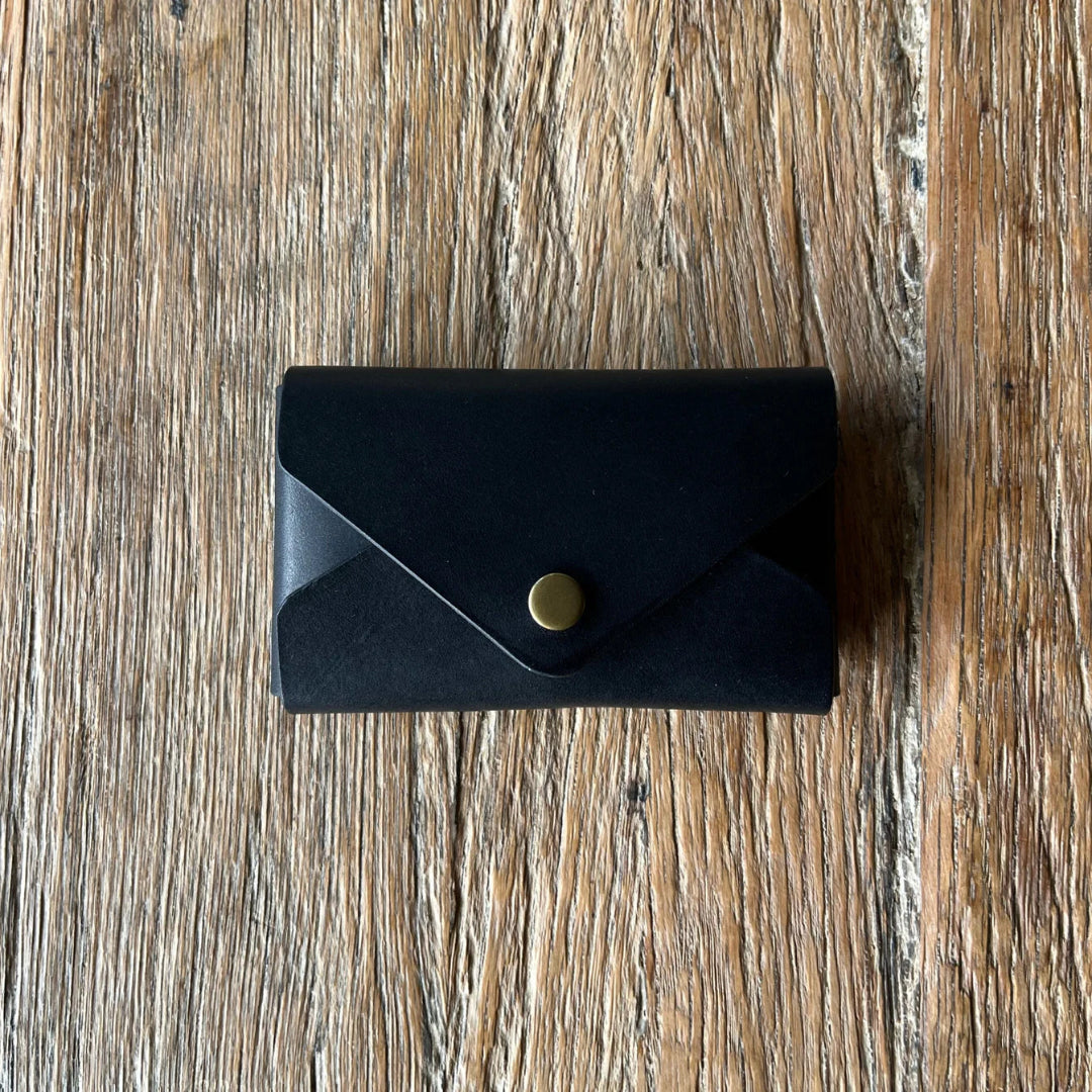 Black leather wallet with a gold button on a wooden surface