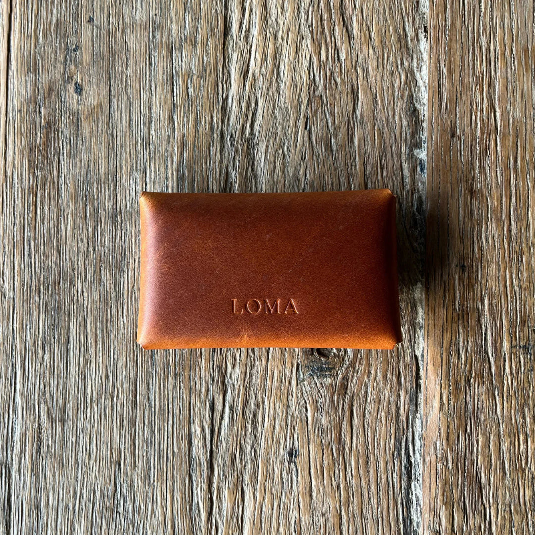 Brown leather wallet with 'LOMA' branding on a wooden surface