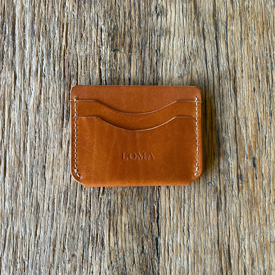 Brown leather cardholder with 'LOMA' branding on a wooden surface