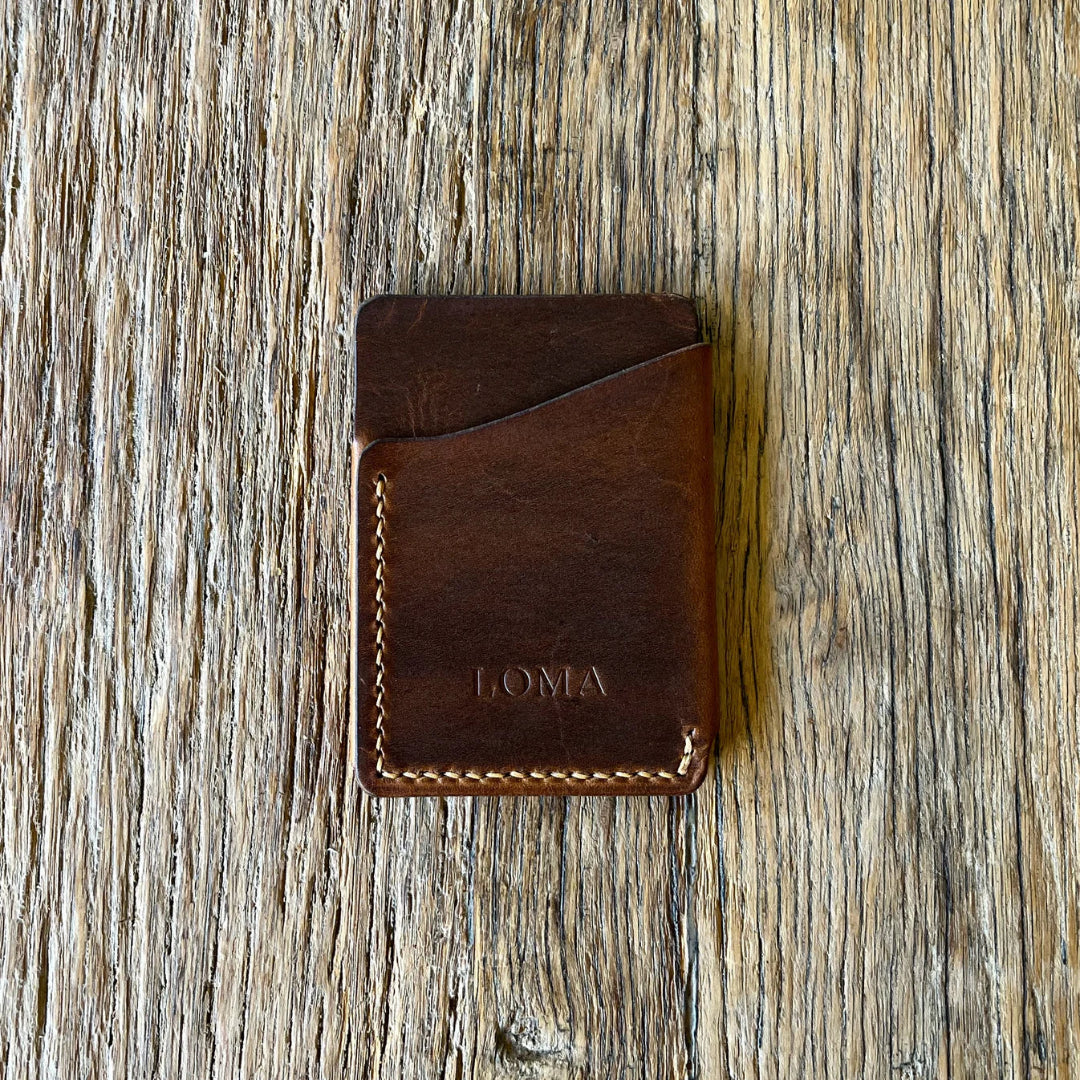 Brown leather wallet with 'LOMA' branding on a wooden surface