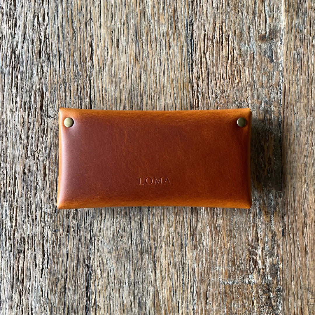 Brown leather wallet with 'LOMA' branding on a wooden surface