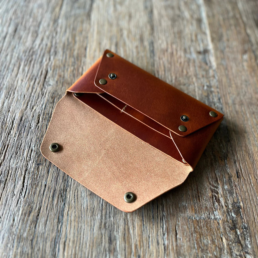 Brown leather wallet with grommets on a wooden surface