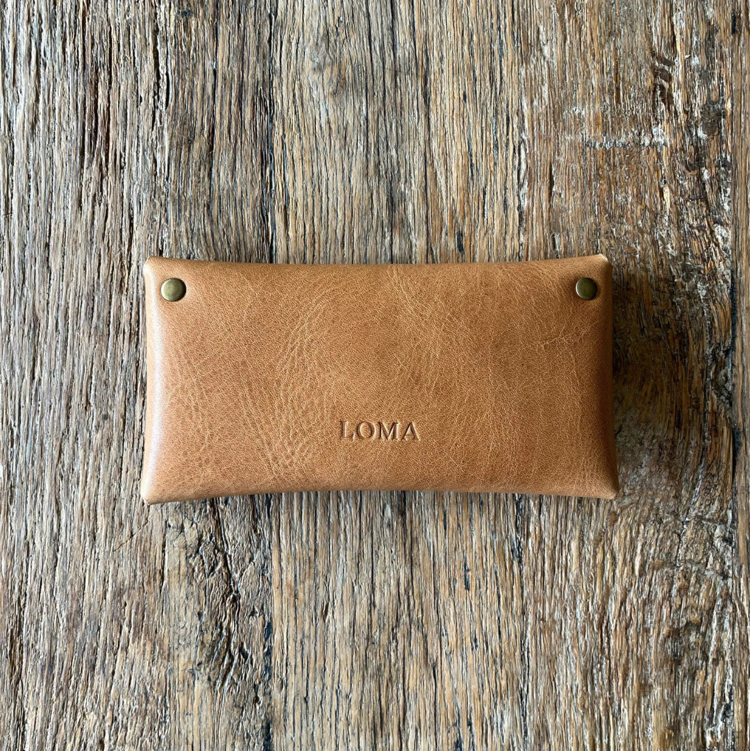 Brown leather wallet with 'LOMA' branding on a wooden surface