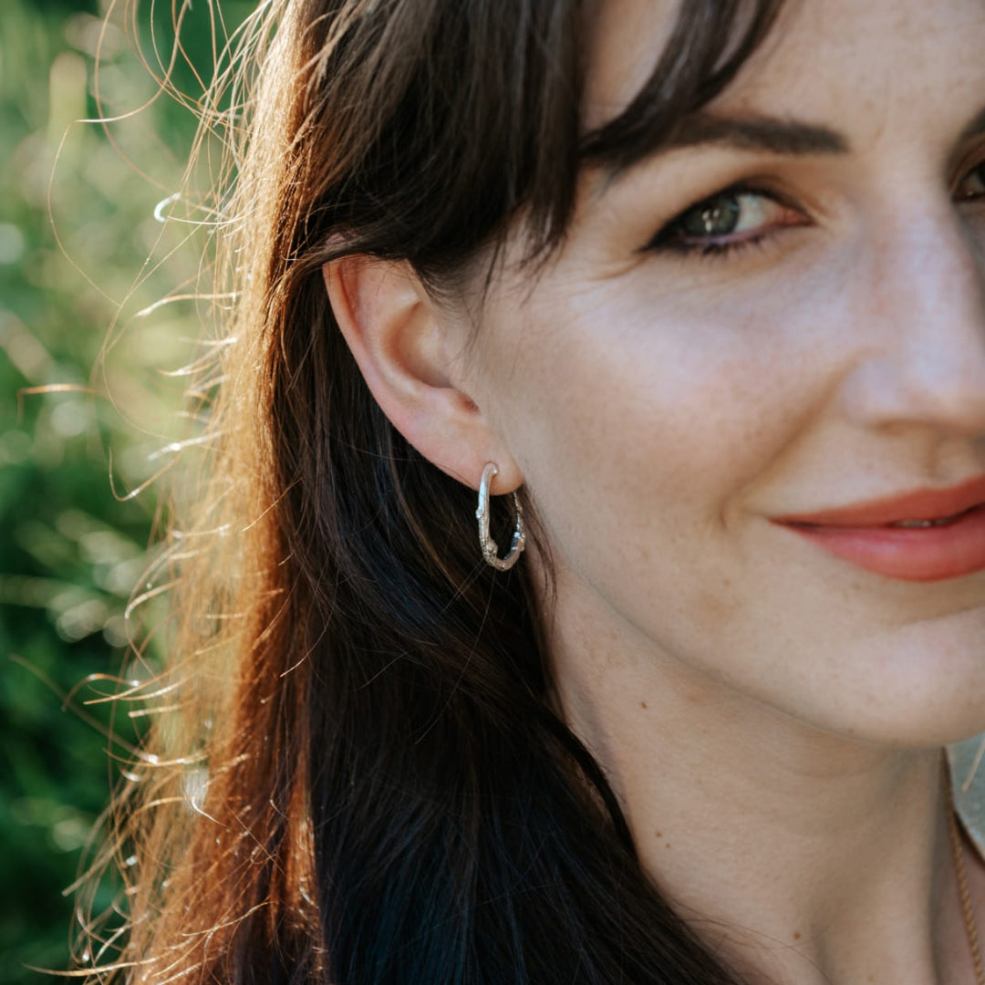 Close-up of a woman wearing a silver hoop earring with a blurred green background