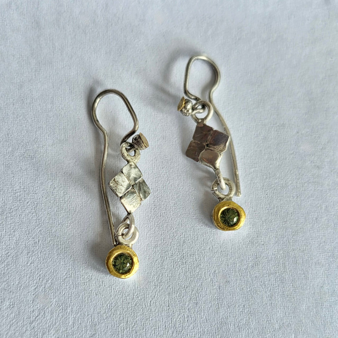 Pair of silver and gold earrings with green sapphires on a light gray background