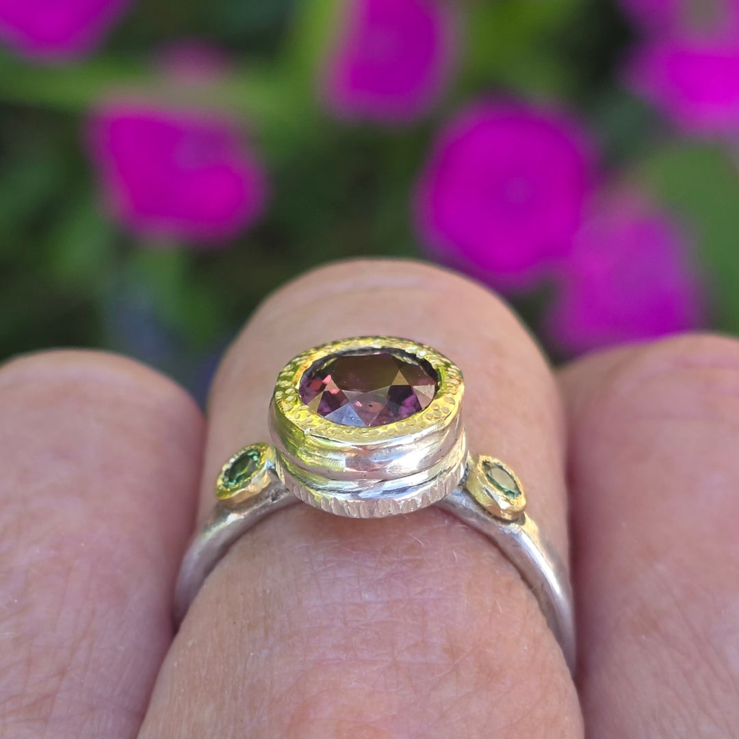 Ring with a red zircon gemstone & green sapphires on a finger against a blurred natural background