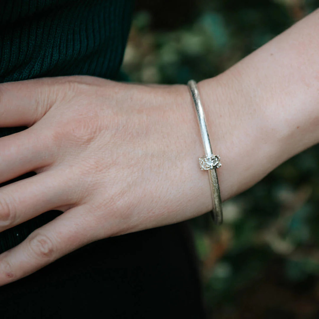 Close-up of a wrist wearing a silver bracelet with a blurred natural background