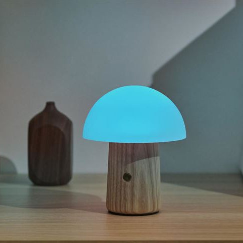 Mushroom-shaped night light emitting a blue glow on a wooden surface with vases in the background.