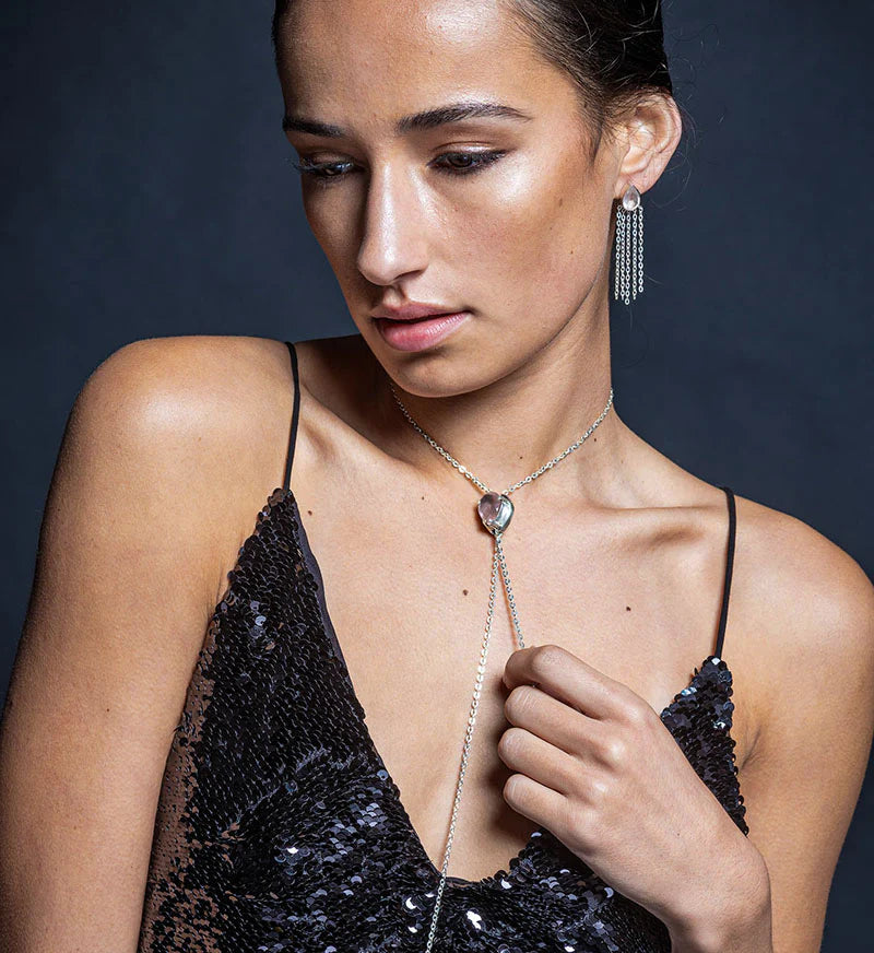 Woman wearing a black sequin dress with a silver necklace and earrings against a dark background