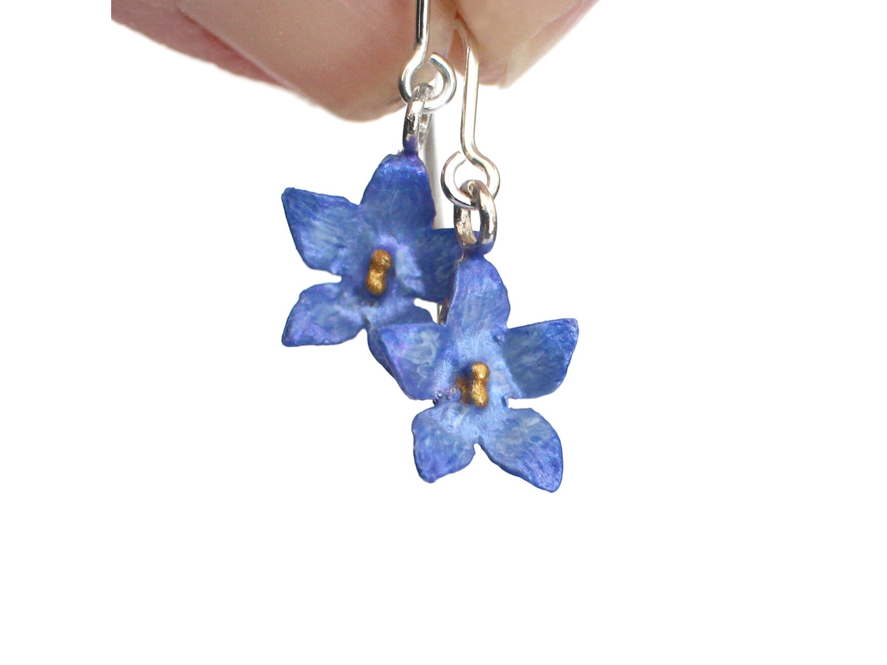 Hand held Blue flower-shaped earrings with silver ear hooks on a white background
