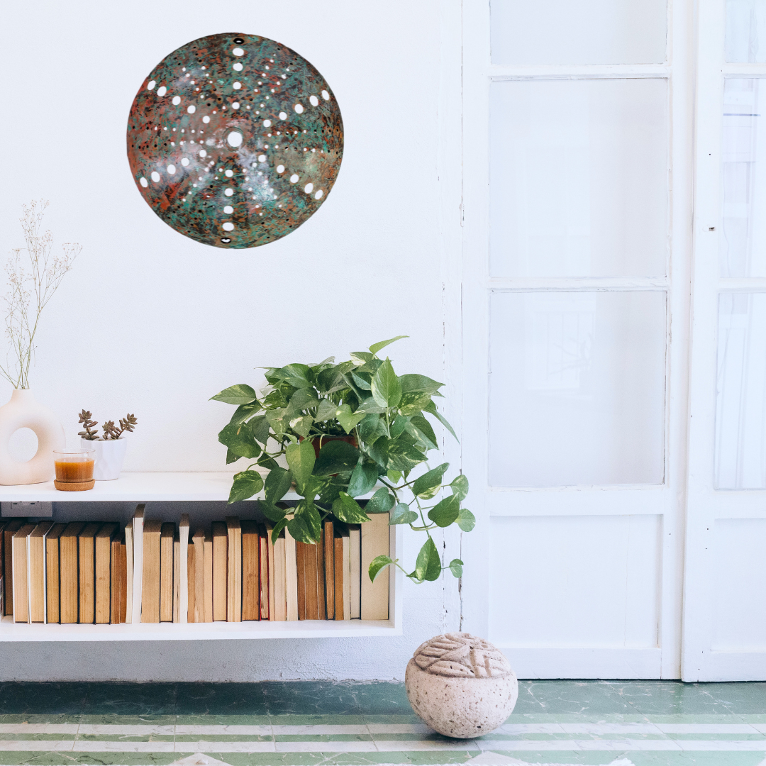 Copper kina sculpture wall art above a bookshelf with a plant on a white wall.