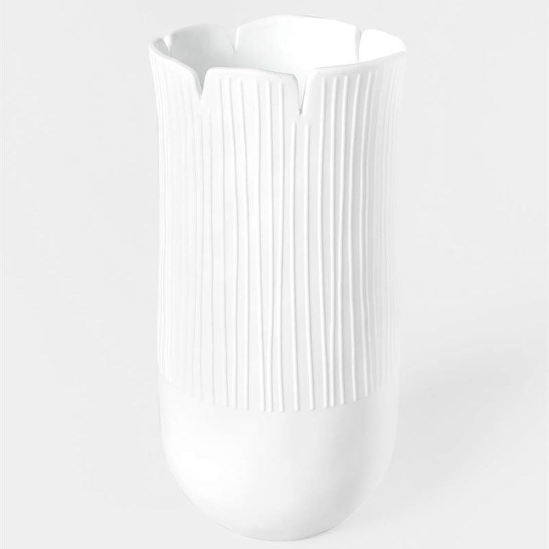A white ceramic vase with a flared, scalloped rim and vertical ribbed texture on the body, set against a seamless light gray background.