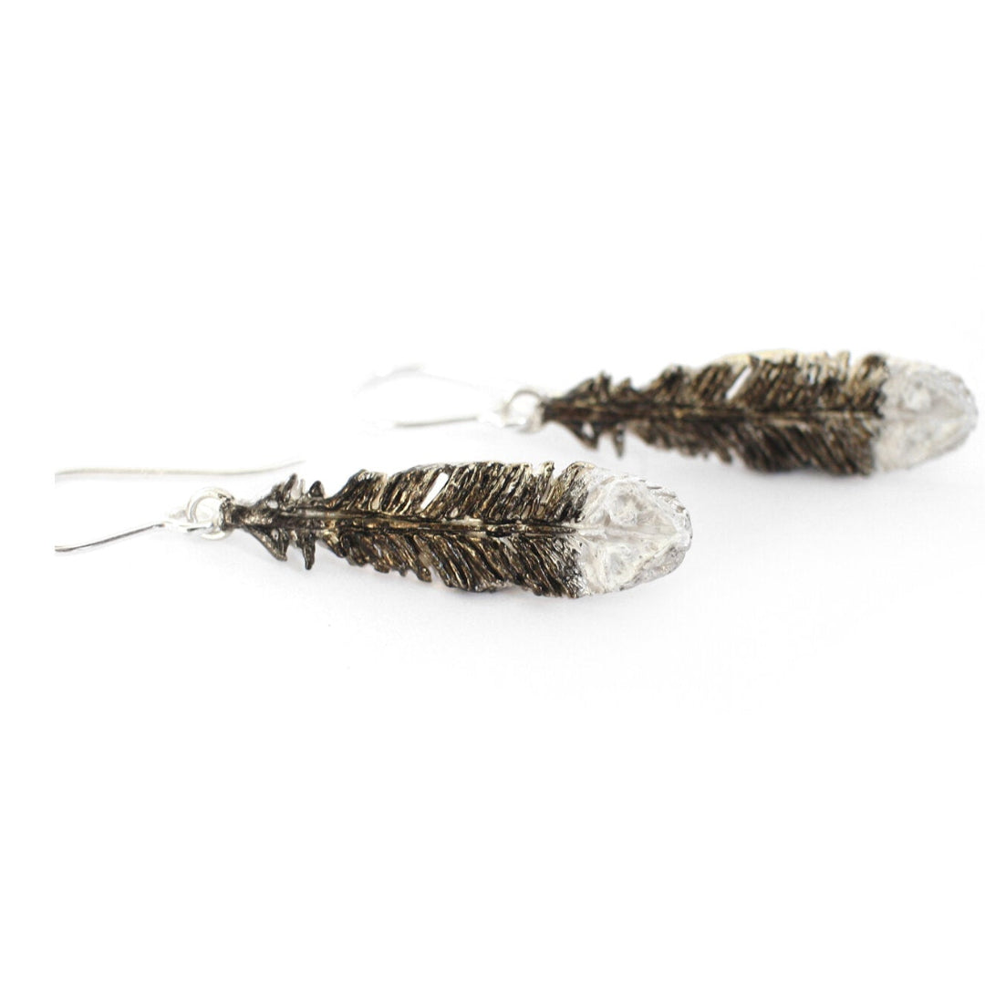 Pair of black and white painted silver Huia feather earrings on a white background background