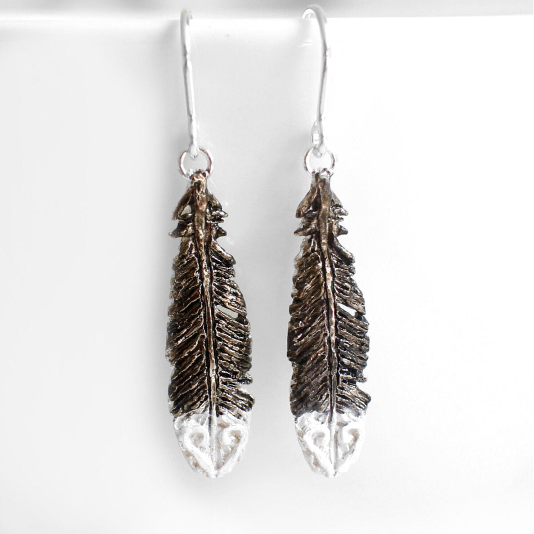 Pair of black and white painted silver Huia feather earrings on a white background background