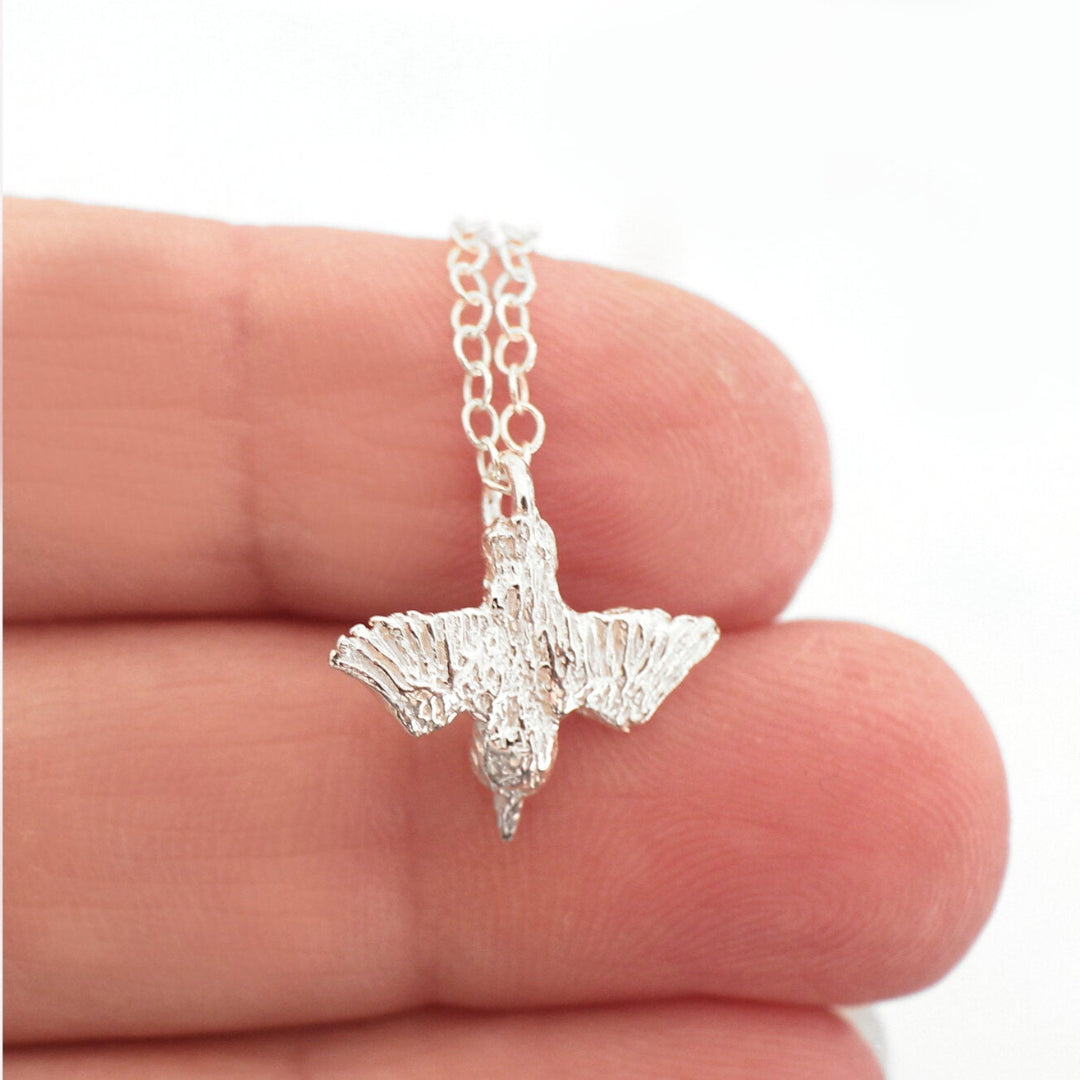 Shiny Silver Diving Kingfisher pendant on a chain held in fingers on a white background