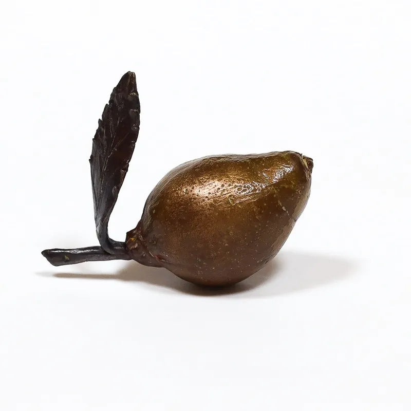 Bronze sculpture of a miniature lemon with leaves on a white background