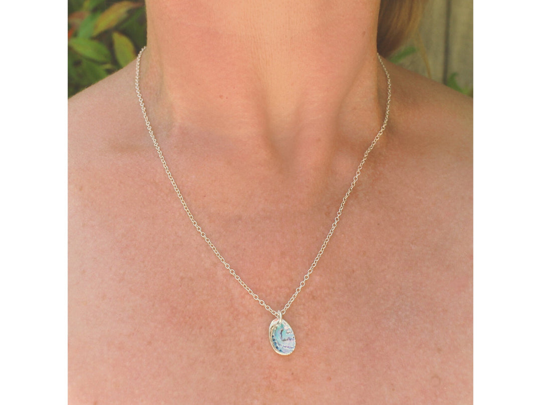 Multicoloured Paua Shell Pendant Necklace with a silver chain worn by a person, with a blurred background