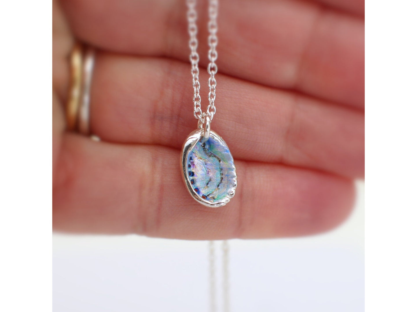 Multicoloured Paua Shell pendant silver necklace held between fingers on a white background