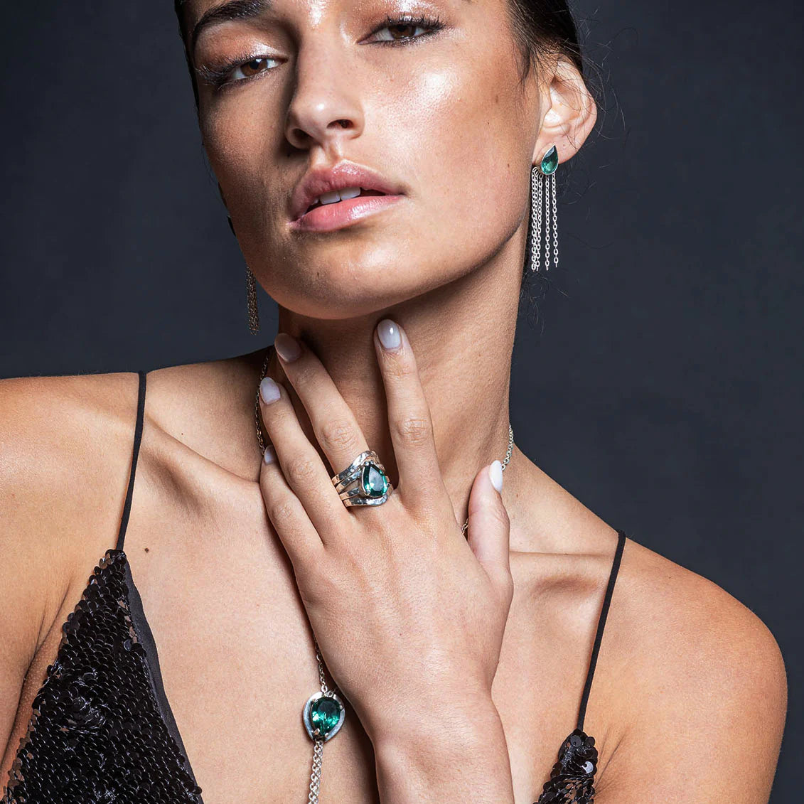 Woman wearing jewelry including earrings, a ring, and a necklace against a dark background