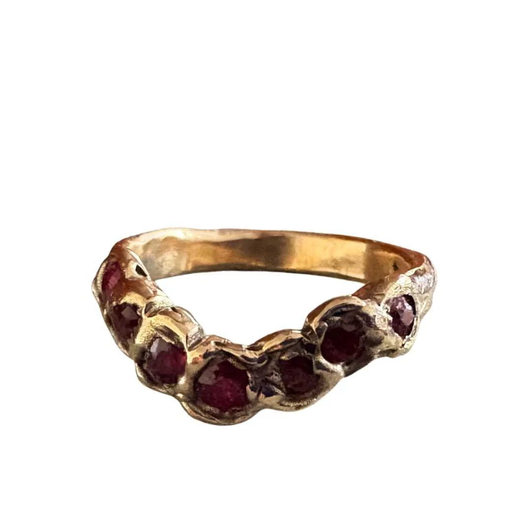 A vintage-style gold ring featuring a row of round-cut dark red gemstones, set against a plain white background.