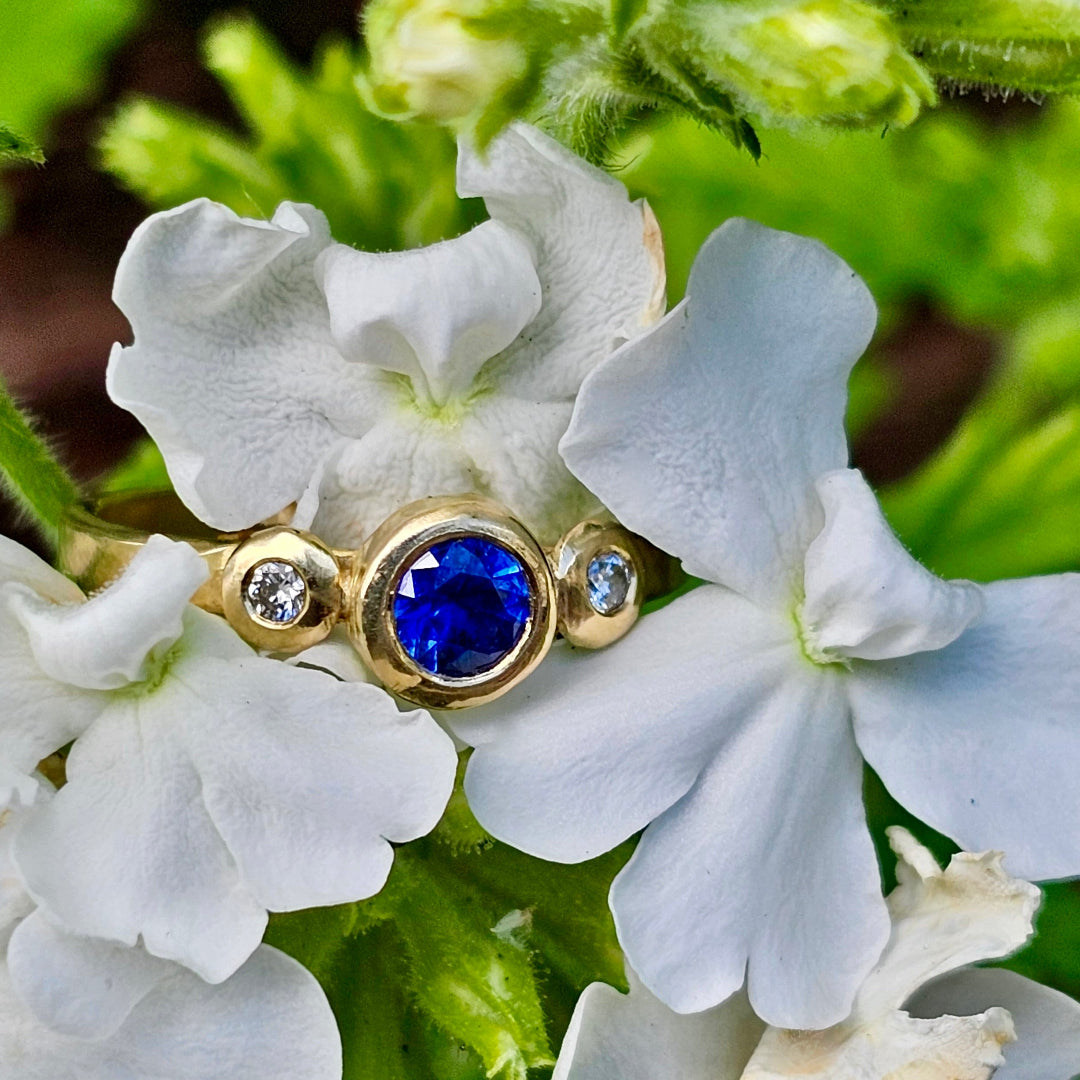 Gold ring with a blue sapphire gemstone & diamonds on a white flower